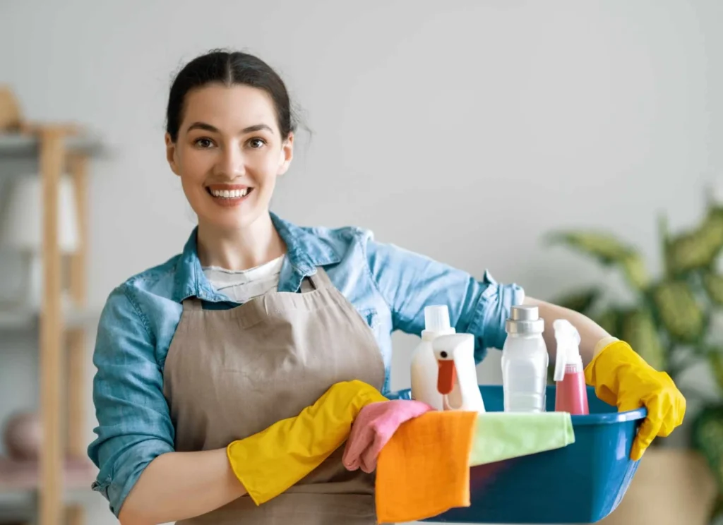 Aide ménagère souriante tenant une bassine de produits d’entretien