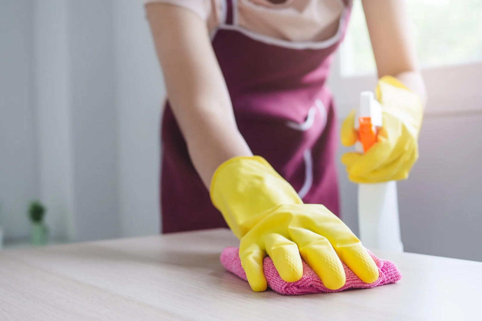 Mains gantées nettoyant une table avec une éponge et un spray