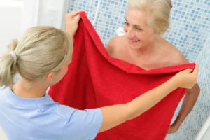 Aide à domicile tendant une serviette à une femme âgée après la douche