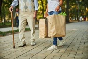 Personne âgée avec une canne et aide portant des sacs de courses